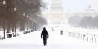A man walks along the National Mall as snow falls in Washington, DC.
