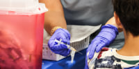 A child is seen from behind while being vaccinated by a nurse on his left arm.