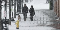 People walk through the snow with a dog outside